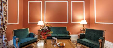 Una habitación con dos sofás verdes, una mesa de centro con fruta y dos lámparas.