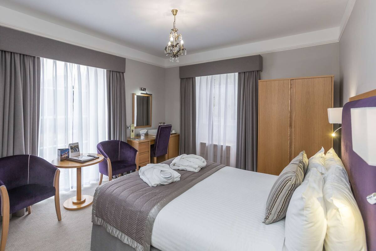 A hotel room with a bed, a desk, a chair, a wardrobe, and a chandelier.