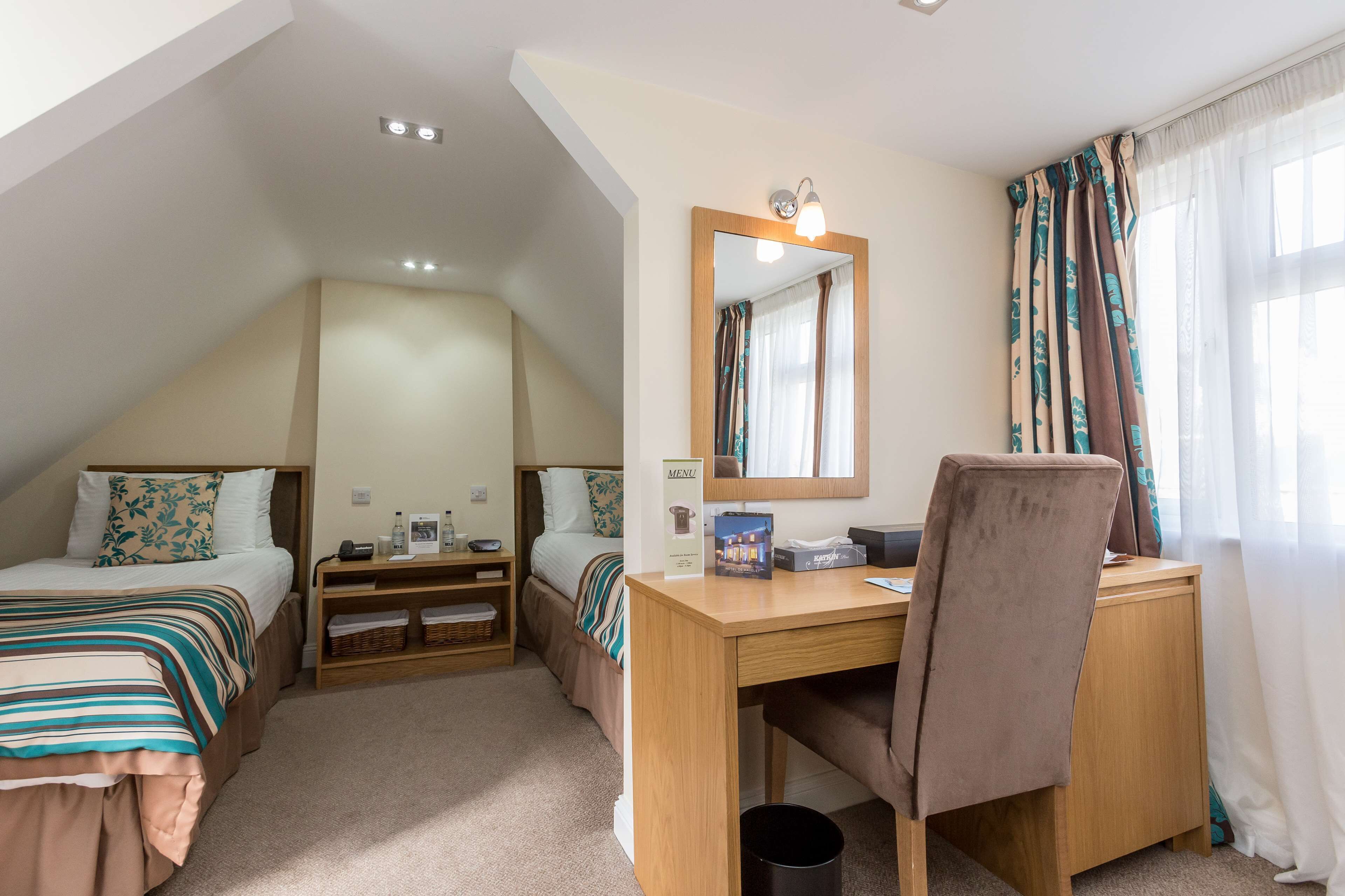 A bedroom with two beds, a desk, a chair, a mirror, and a window with curtains.
