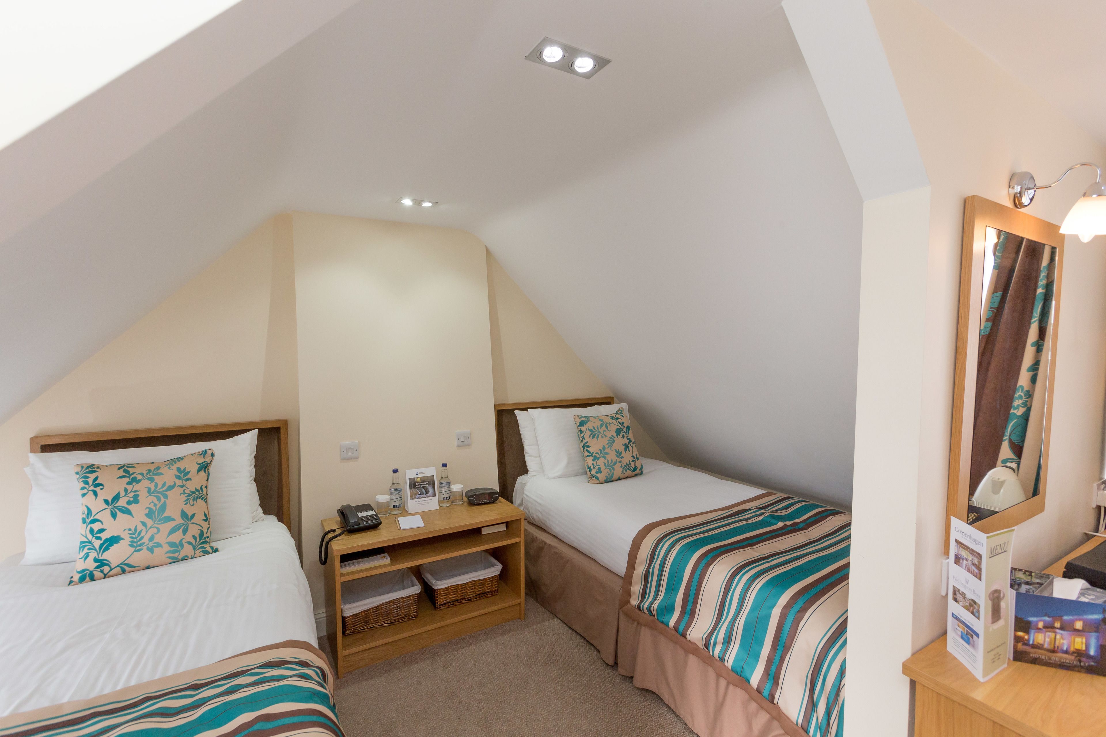 A bedroom with two beds, a wooden nightstand, a mirror, and a ceiling light.