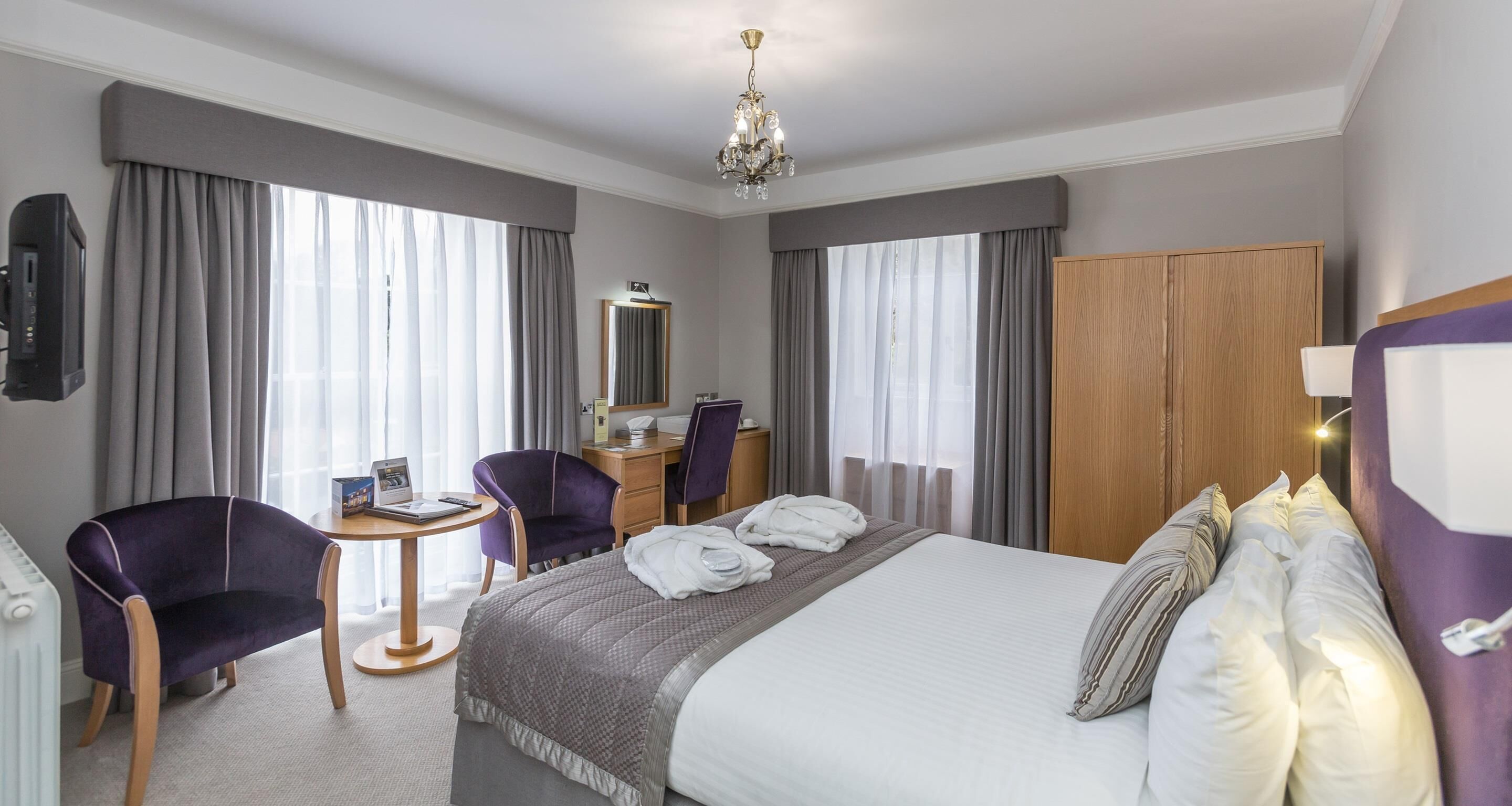 Una habitación de hotel con cama, escritorio, silla, armario y televisor.