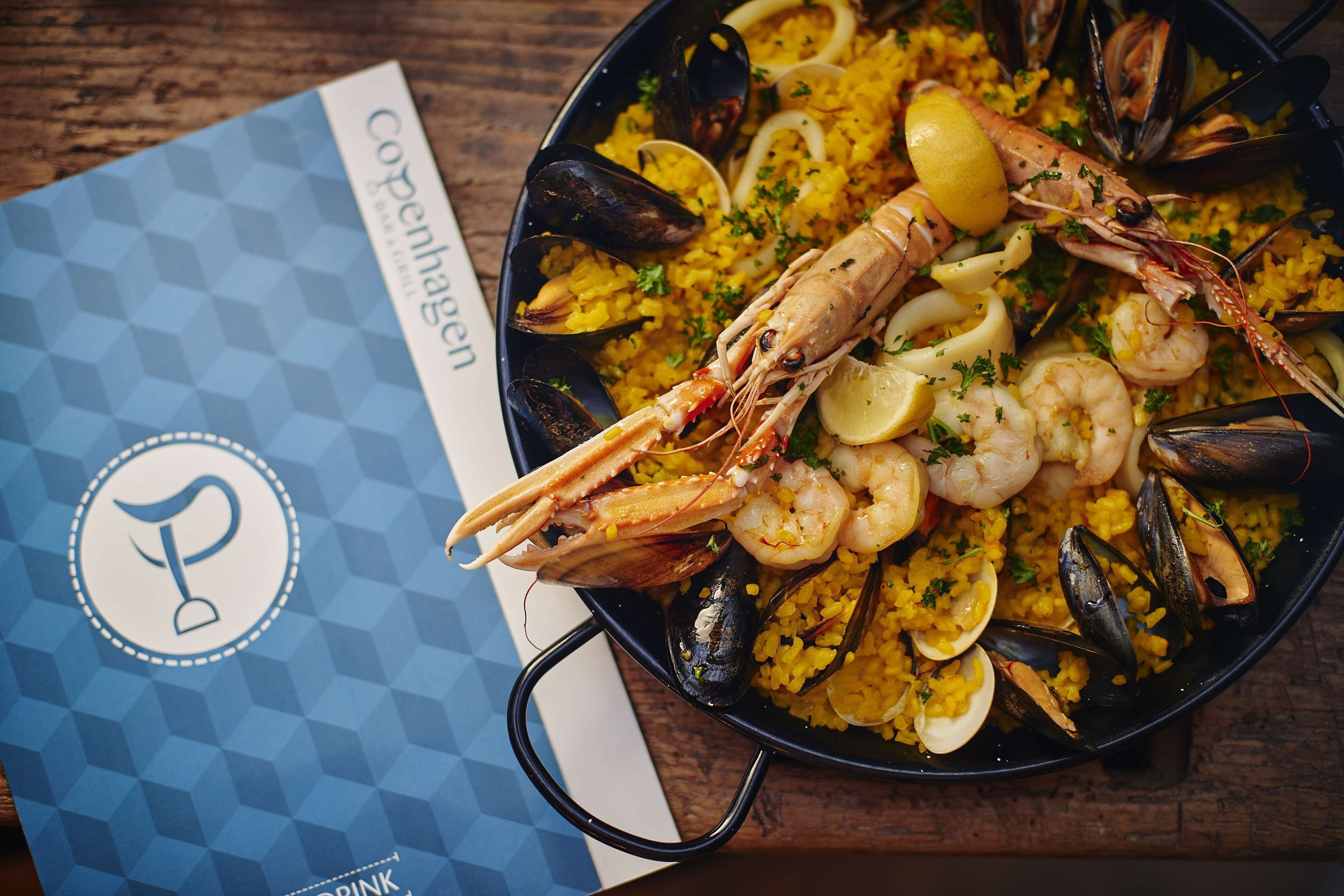 Un plato de mariscos con mejillones, camarones y rodajas de limón sobre una mesa de madera.