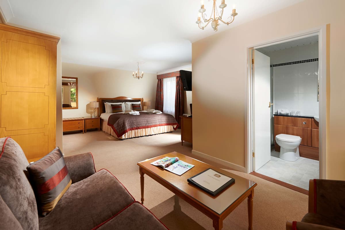 A hotel room with a bed, a sitting area with a table and chairs, a wardrobe, and a bathroom visible through an open door.