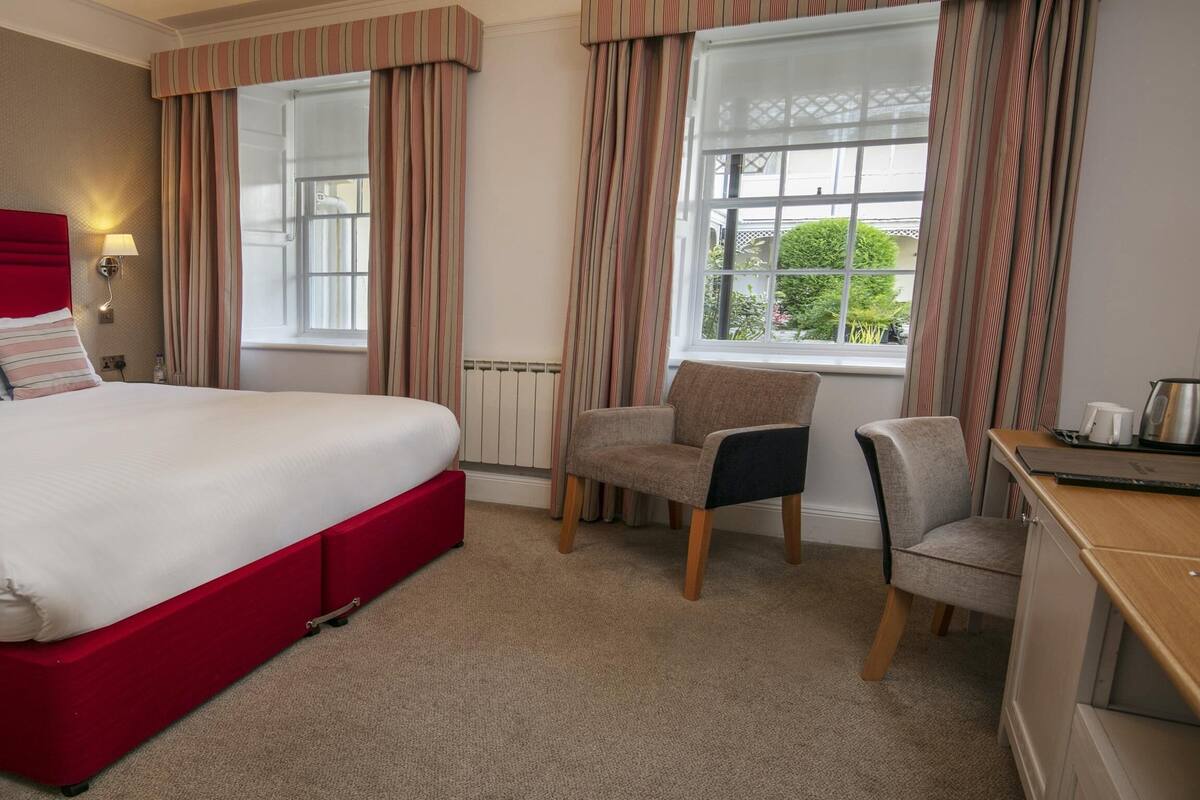 A hotel room with a red bed, striped curtains, a chair, and a desk.
