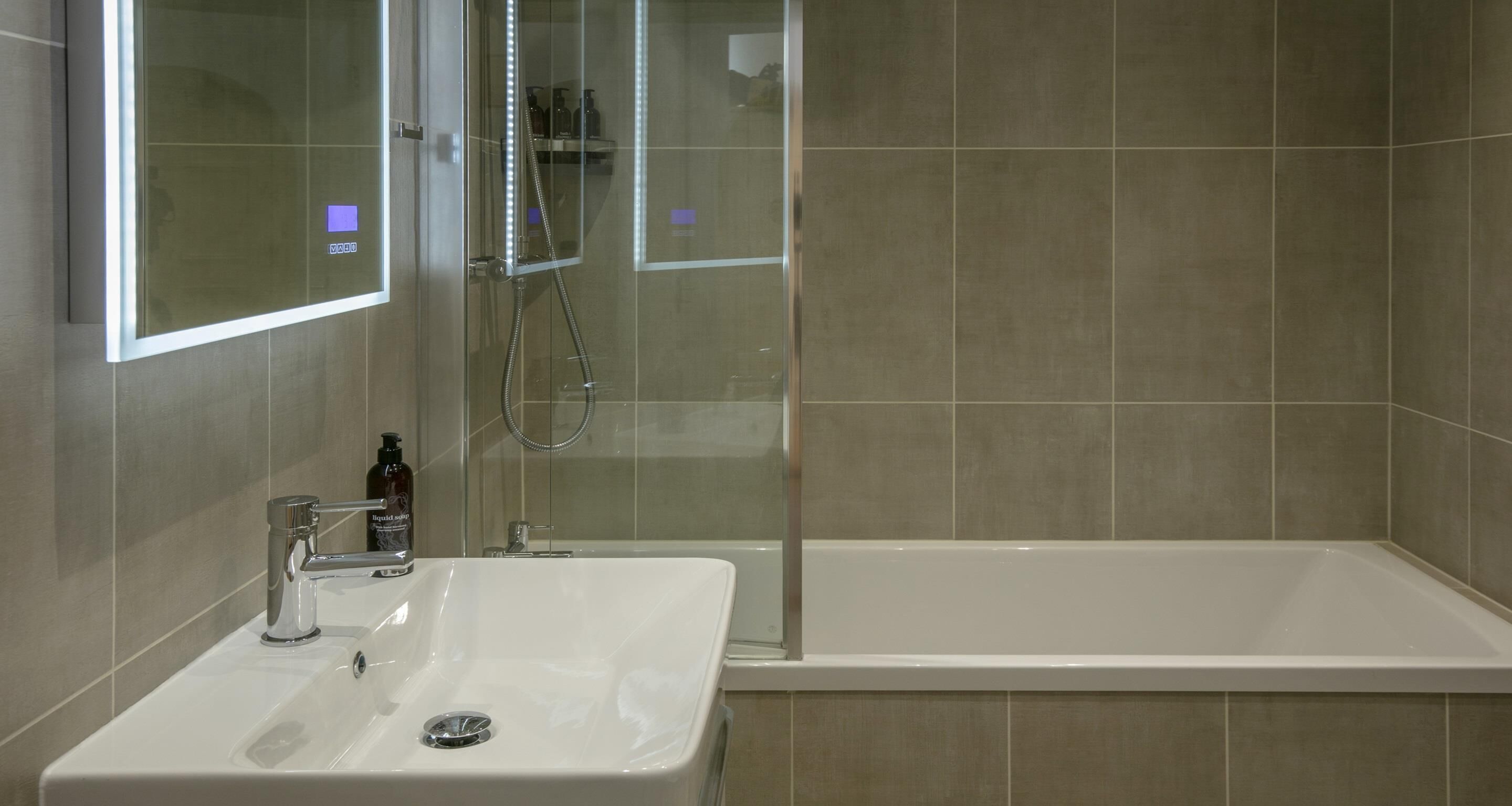 Baño con lavamanos, espejo y cabina de ducha.