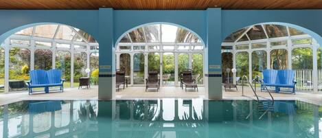 An indoor swimming pool with clear blue water, wooden ceiling, and three arched windows.