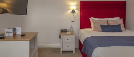 Una habitación de hotel con cama, mesita de noche, lámpara, televisor y escritorio con control remoto.