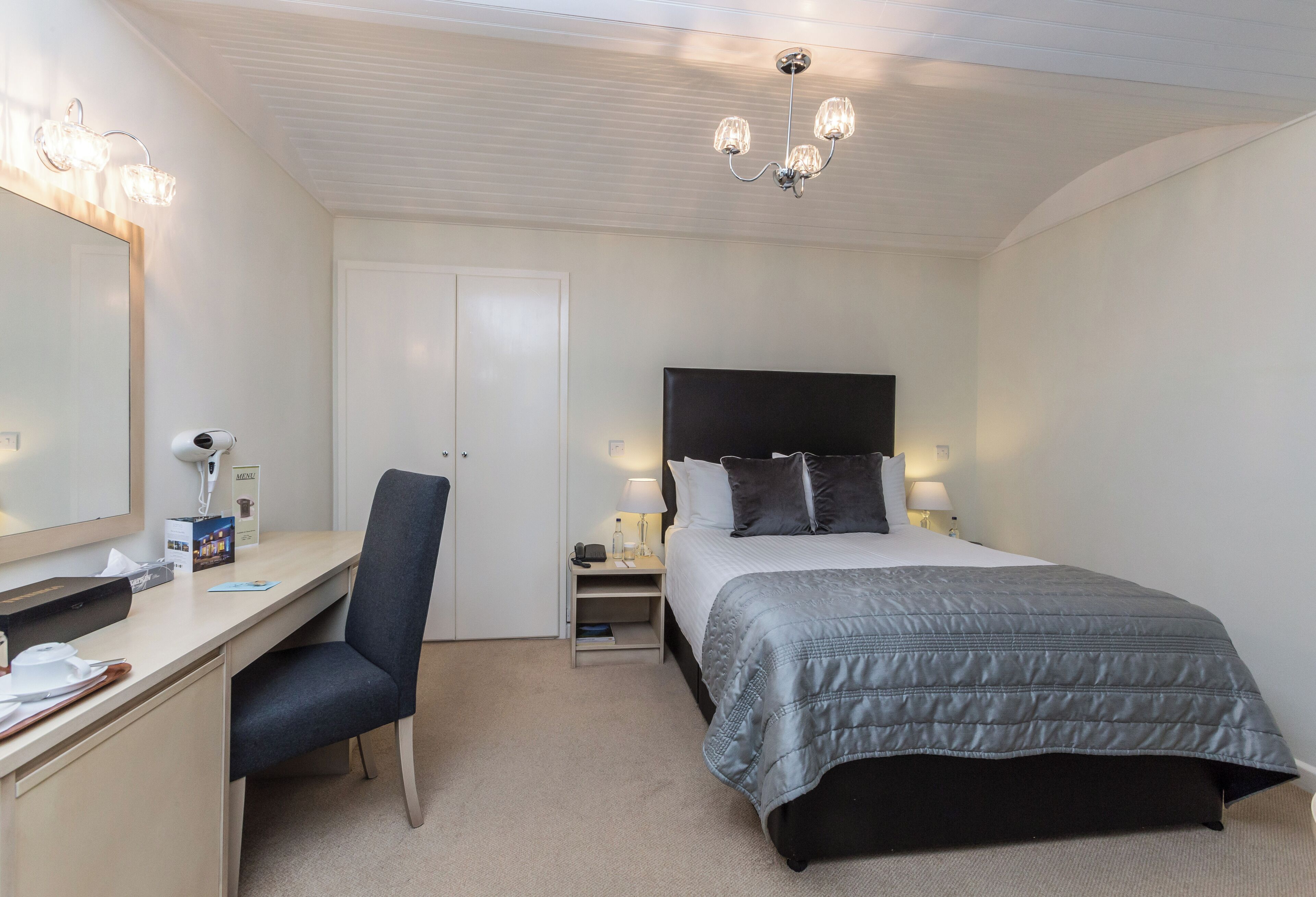 A hotel room with a bed, desk, chair, and a large mirror.