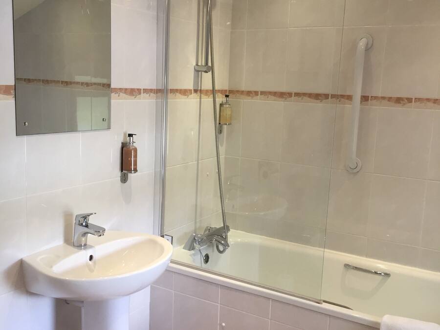 Un bagno moderno con doccia vetro, lavabo su piedistallo e un ampio specchio.