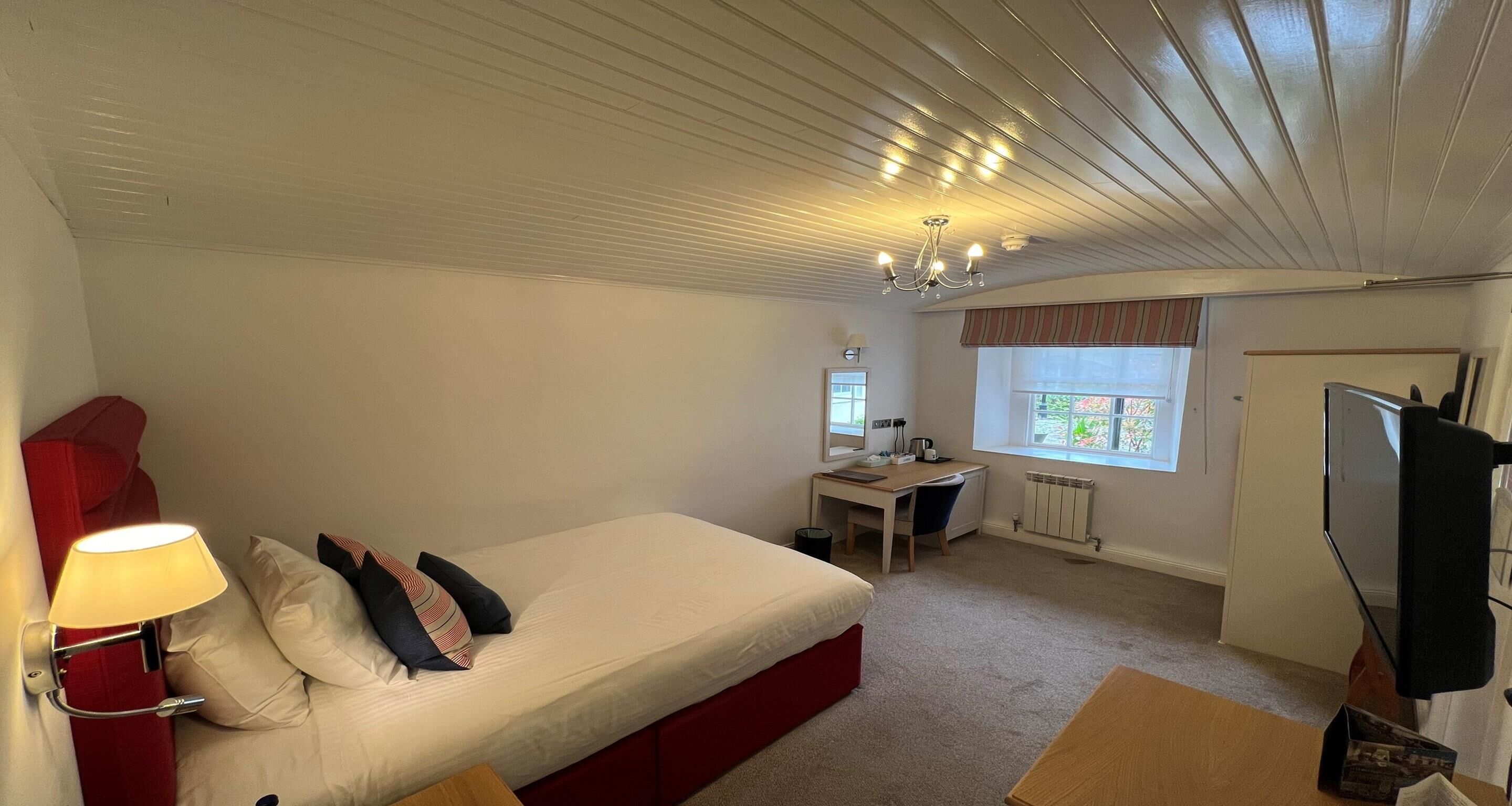 A bedroom with a bed, desk, chair, and a television.