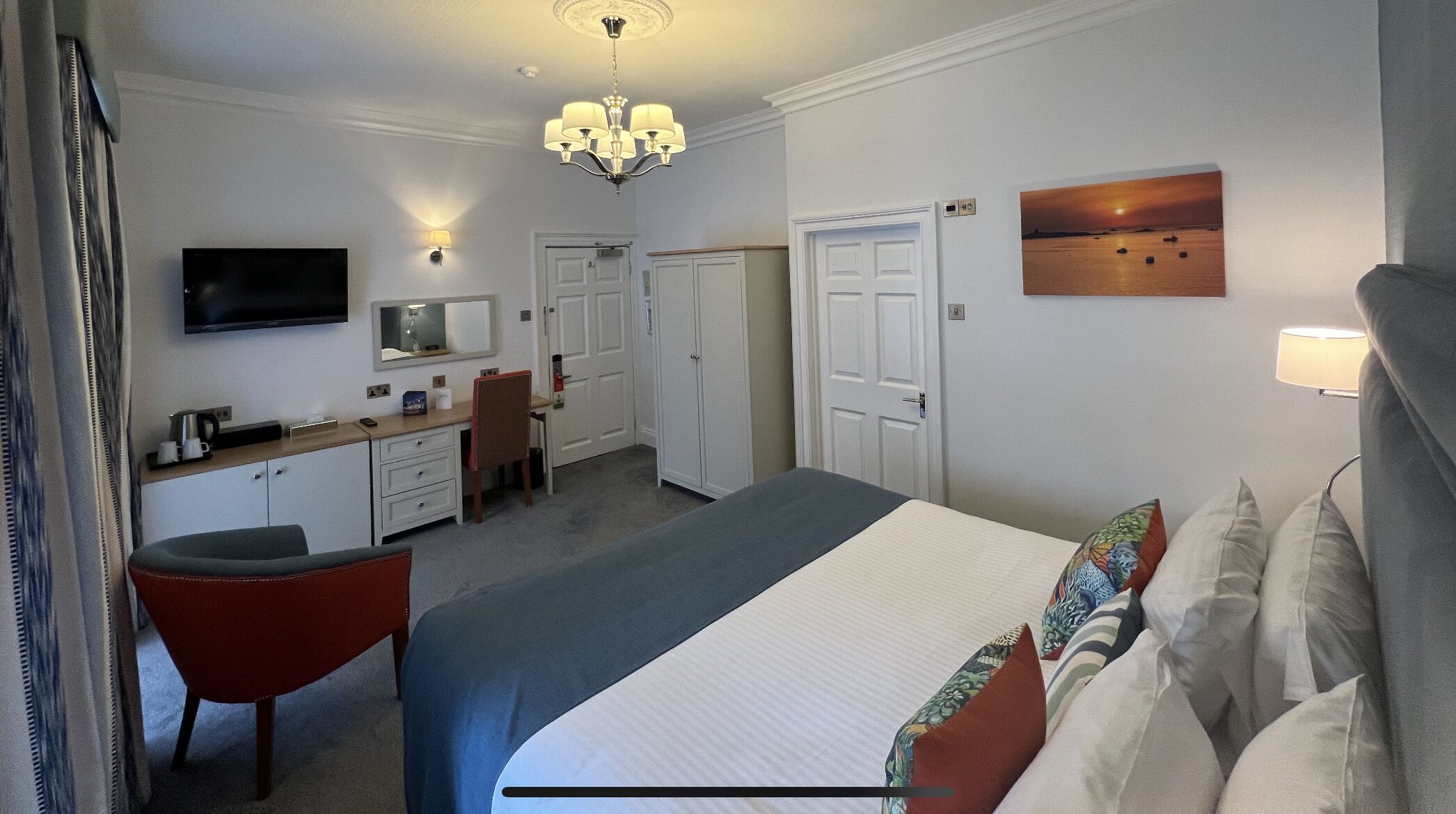 A hotel room with a bed, a desk, a chair, a TV, and a painting on the wall.