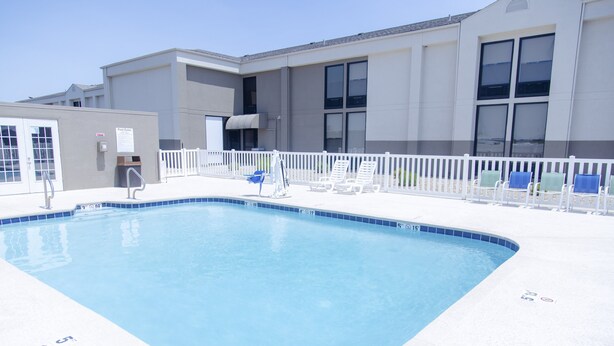 A swimming pool with a white fence and lounge chairs.