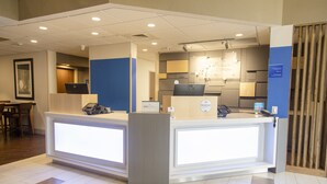 A hotel reception desk with a computer, a phone, and a sign indicating a 24-hour service.