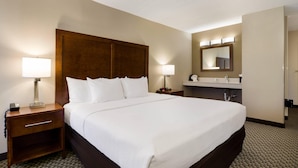 A hotel room with a large bed, a wooden headboard, a nightstand with a lamp, a bathroom with a mirror and lights, and a carpeted floor. - Comfort Inn Lexington Virginia Horse Center (Lexington)