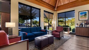 A modern lobby with a blue sofa, red armchair, and a wooden ceiling. Large windows offer views of the outdoors. - Comfort Inn Lexington Virginia Horse Center (Lexington)