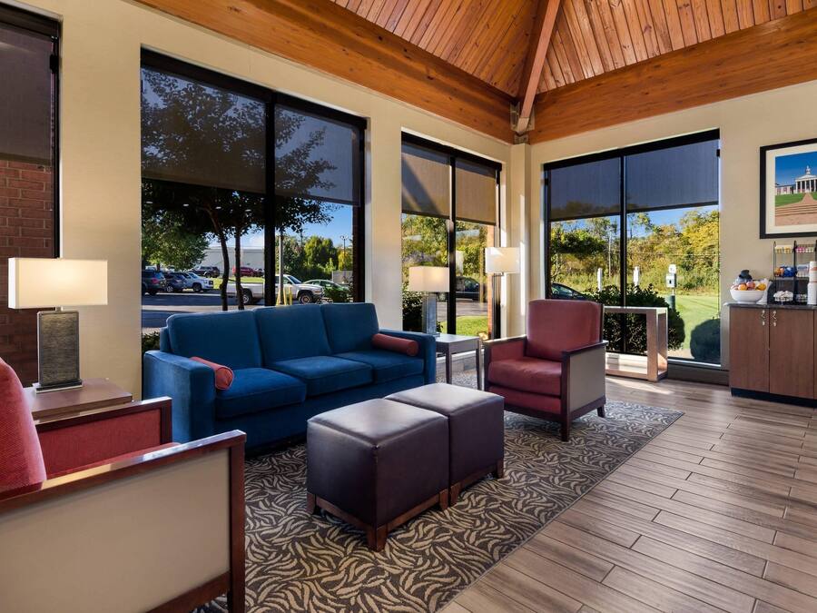 Un vestíbulo moderno con un sofá azul, un sillón rojo y un techo de madera. Amplias ventanas ofrecen vistas del exterior.