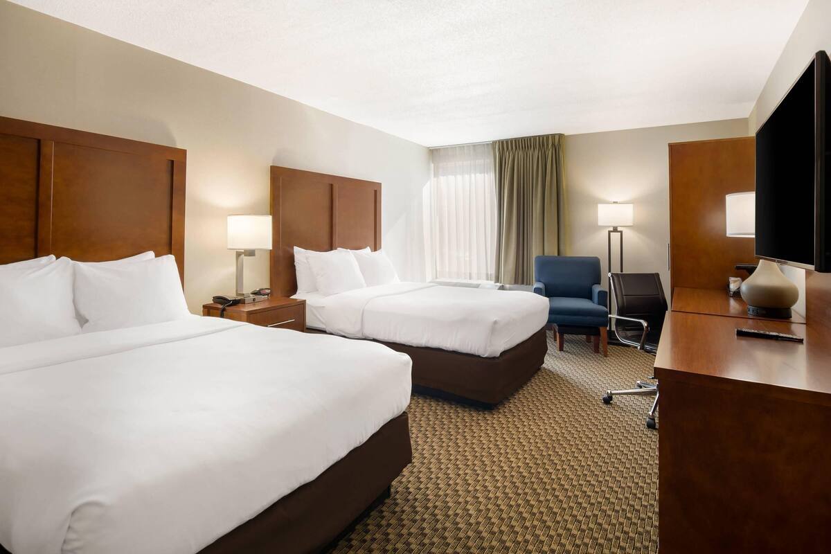 A hotel room with two beds, a desk, a chair, and a TV.