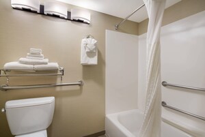 Un baño con inodoro, bañera con cortina de ducha, toallero con toallas dobladas y pasamanos.