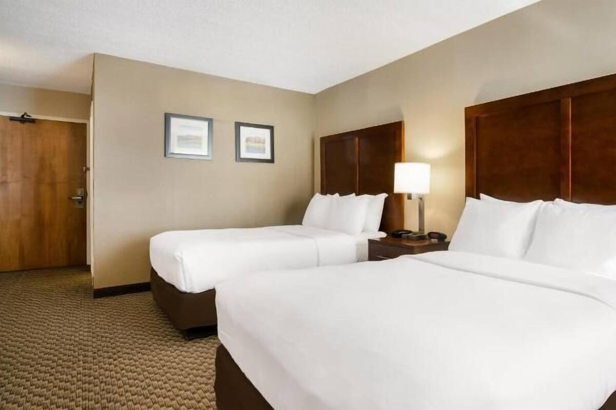 A hotel room with two beds, a wooden headboard, a nightstand with a lamp, and a door.