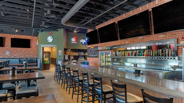 Una zona de bar con una barra larga, varios taburetes y una selección de grifos de cerveza.