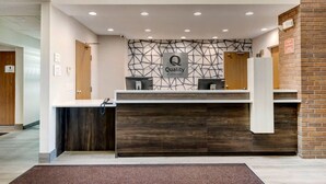 Un mostrador de recepción con un muro de diseño geométrico, un letrero de 'Quality by Choice Hotels' y un diseño moderno con elementos de madera y blanco.