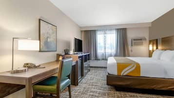 A hotel room with a bed, desk, chair, television, and a painting on the wall.