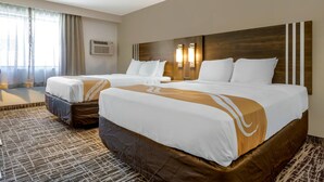 Habitación de hotel con dos camas, un ventanal con cortinas, aire acondicionado de pared y alfombra estampada.