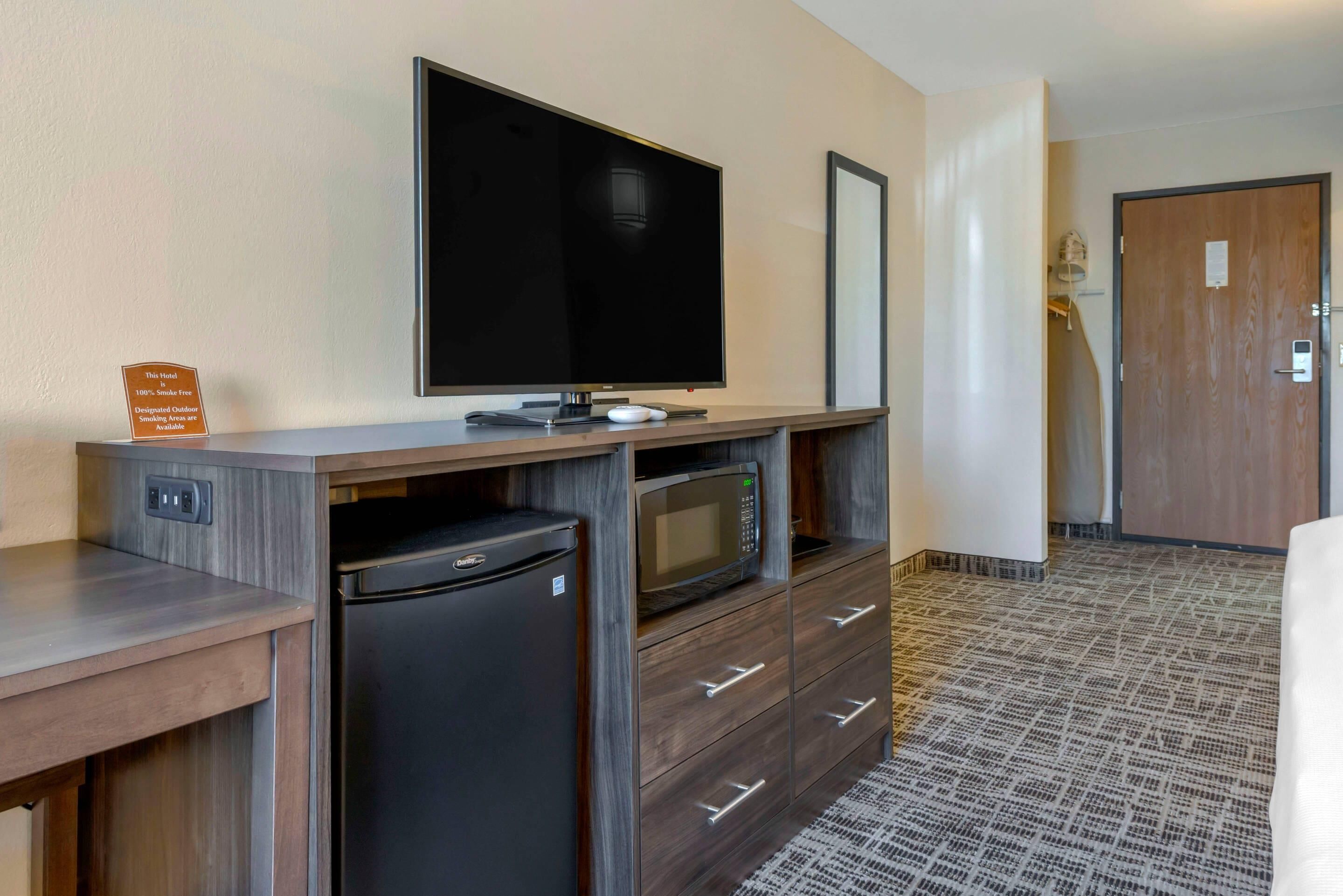 Habitación de hotel con televisión de pantalla plana, microondas, mini refrigerador y escritorio de madera.