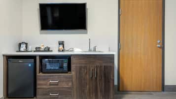 Una kitchenette compacta equipada con microondas, refrigerador, cafetera y un televisor de pantalla plana sobre la encimera.