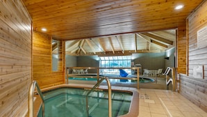 Una piscina interior con paredes de madera y suelo de baldosas, rodeada de zonas de estar y vistas al exterior.