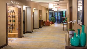 A hotel lobby with a reception desk, a lobby shop, and a seating area with chairs and a potted plant.