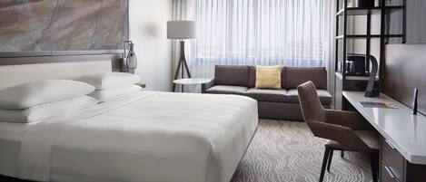 A hotel room with a large bed, a sofa, a desk, and a bookshelf.