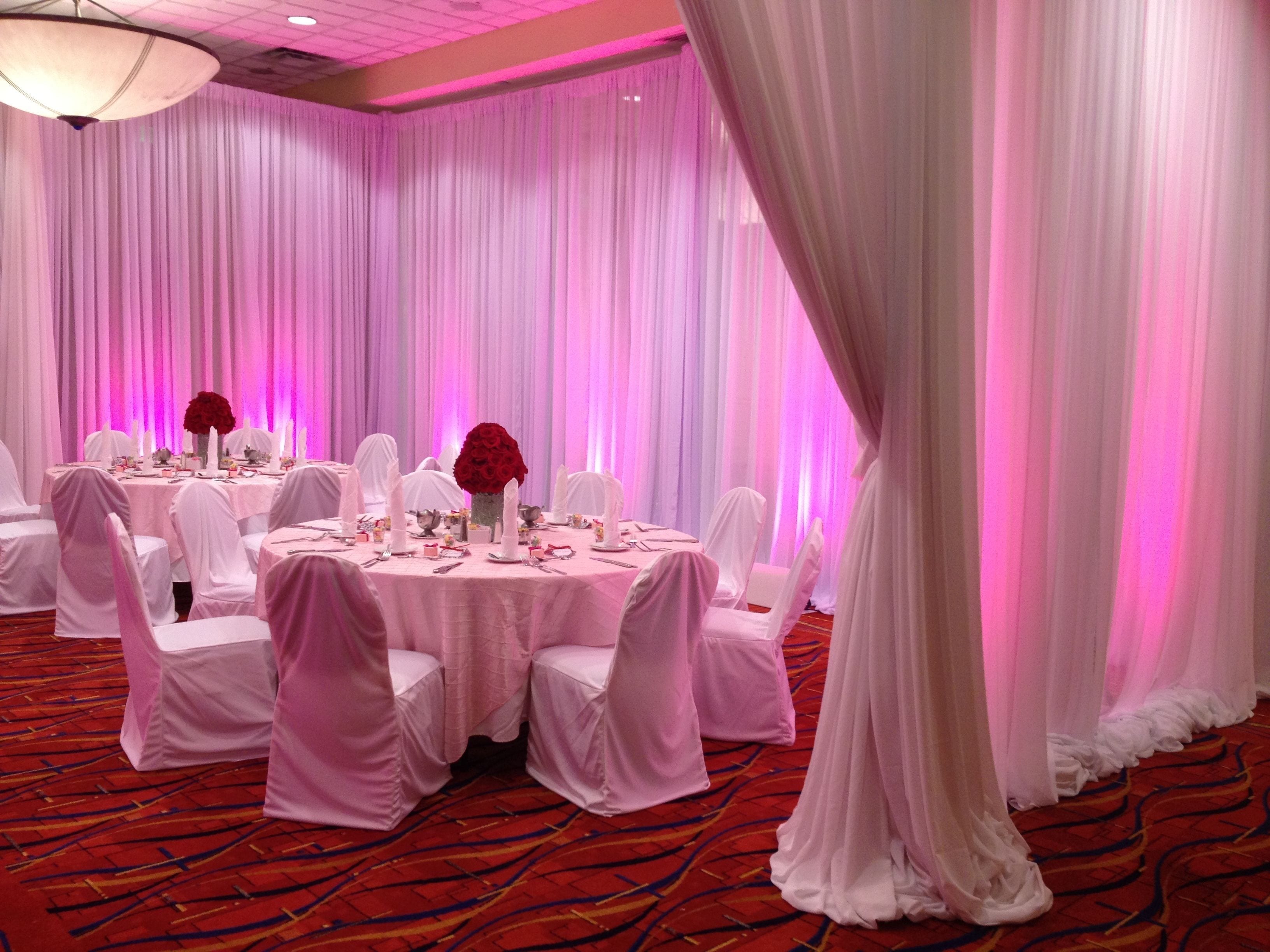 A banquet hall with round tables, white chairs, and pink drapery.