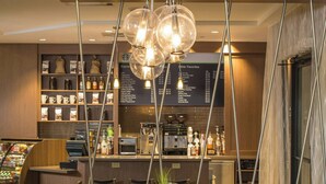 A hotel dining area with a wooden table, chairs, a menu board, and a coffee machine.