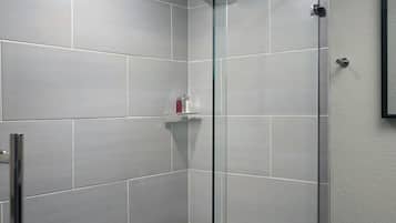 Ein modernes Badezimmer mit einer gläsernen Dusche, grauen Fliesen, einer weißen Toilette und einer Glastür zur Dusche.