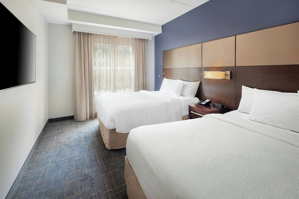 A hotel room with two beds, a flat-screen TV, a nightstand, and a window with curtains.