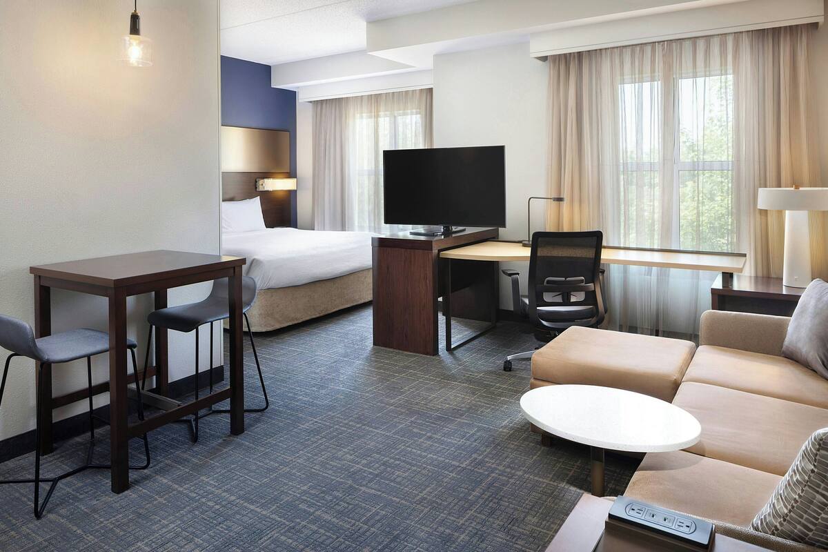 A hotel room with a bed, a desk with a TV, a sofa, a small table, and a chair.