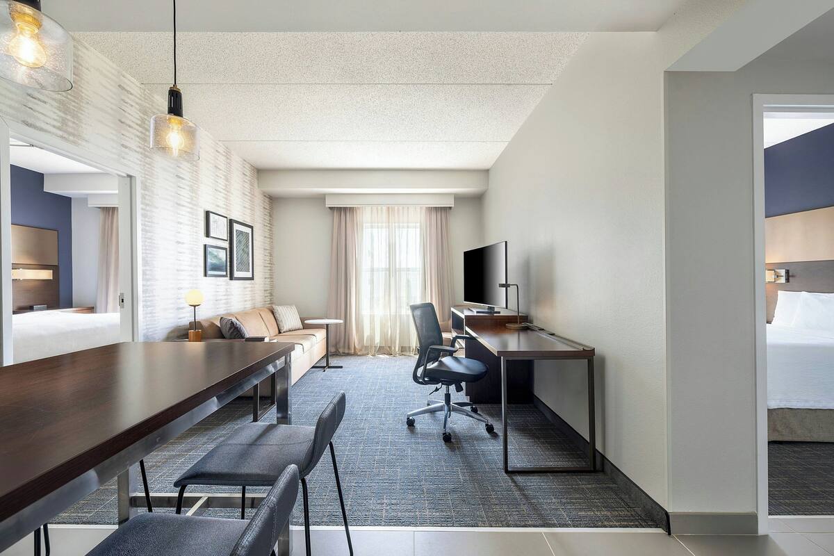 A hotel room with a large bed, a desk with a computer, a chair, a sofa, and a TV.