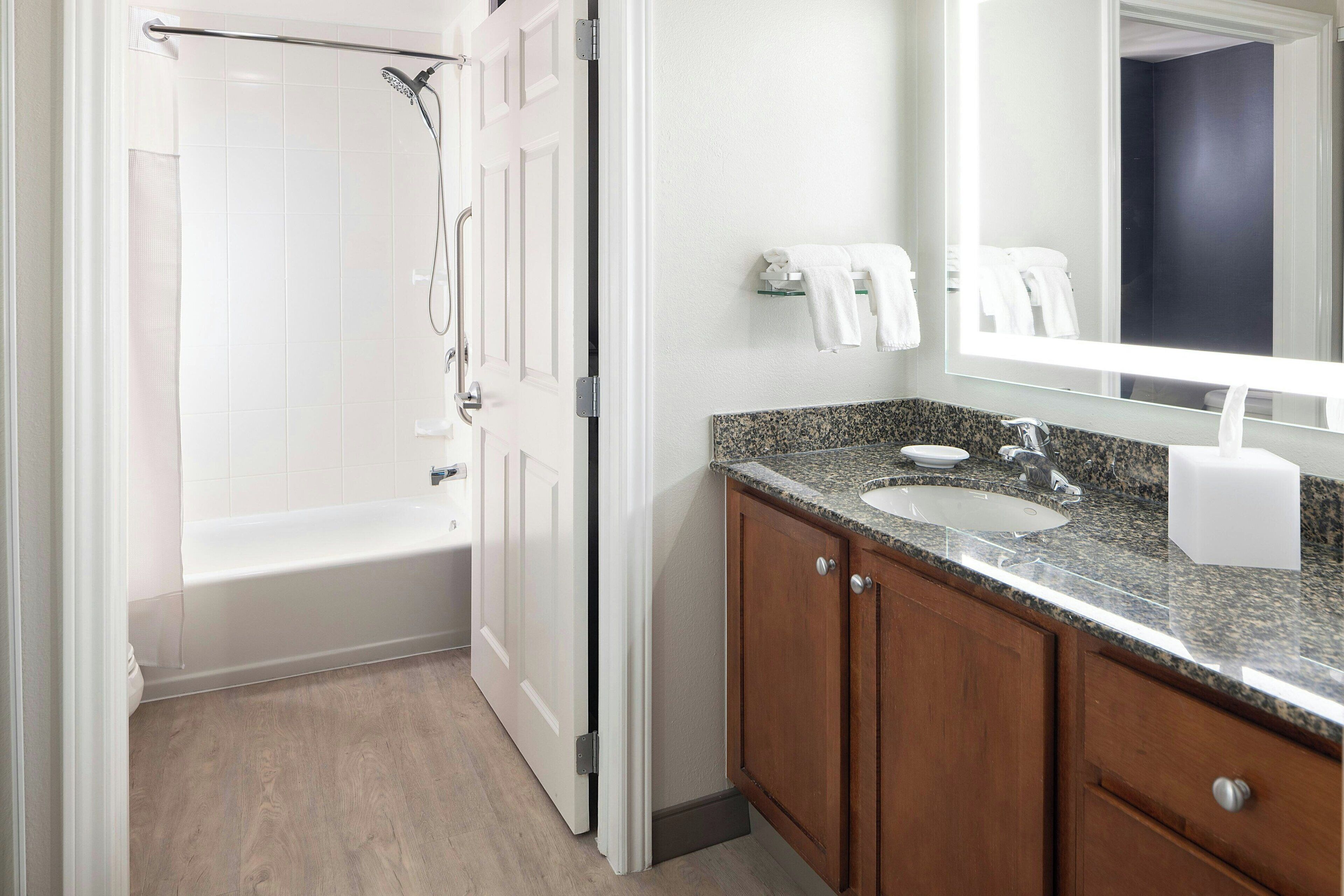 A bathroom with a white bathtub, a sink with a granite countertop, wooden cabinets, and a large mirror.