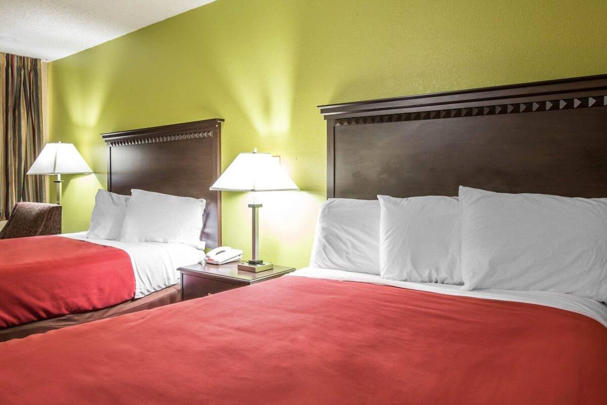 A hotel room with two beds, each with red bedding, a wooden headboard, and a bedside lamp.