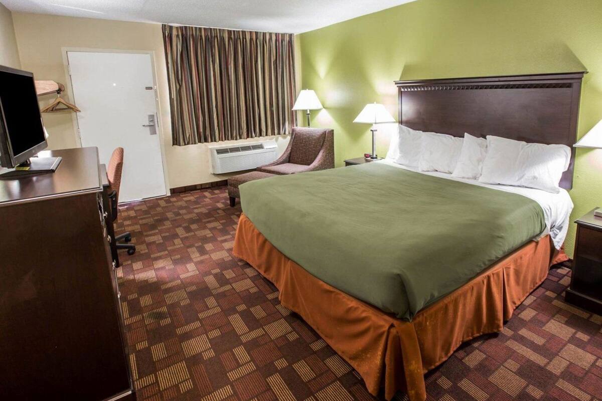 A hotel room with a bed, desk, chair, lamps, and a television.