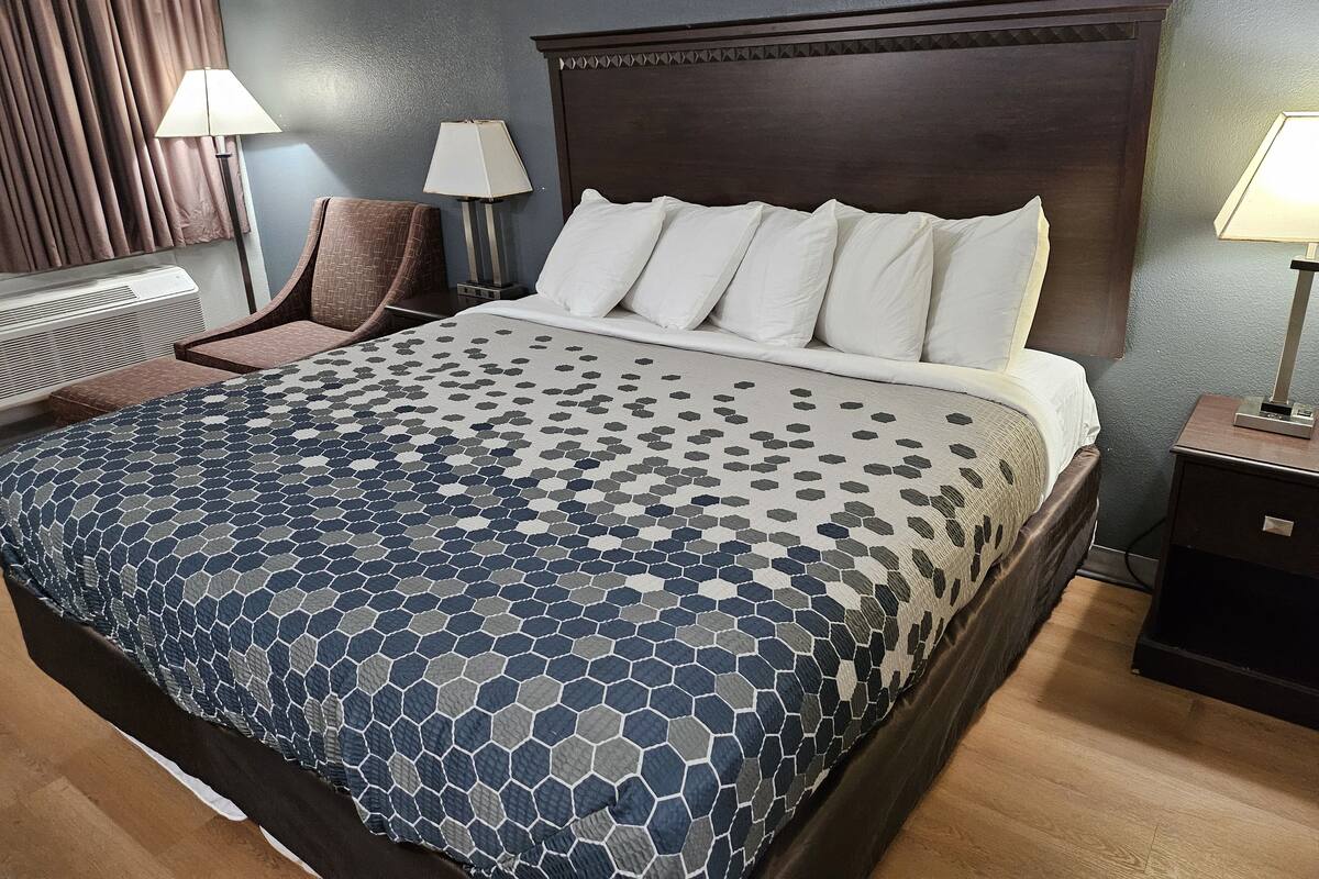 A neatly made bed with a patterned bedspread, a dark wooden headboard, and a bedside table with a lamp.