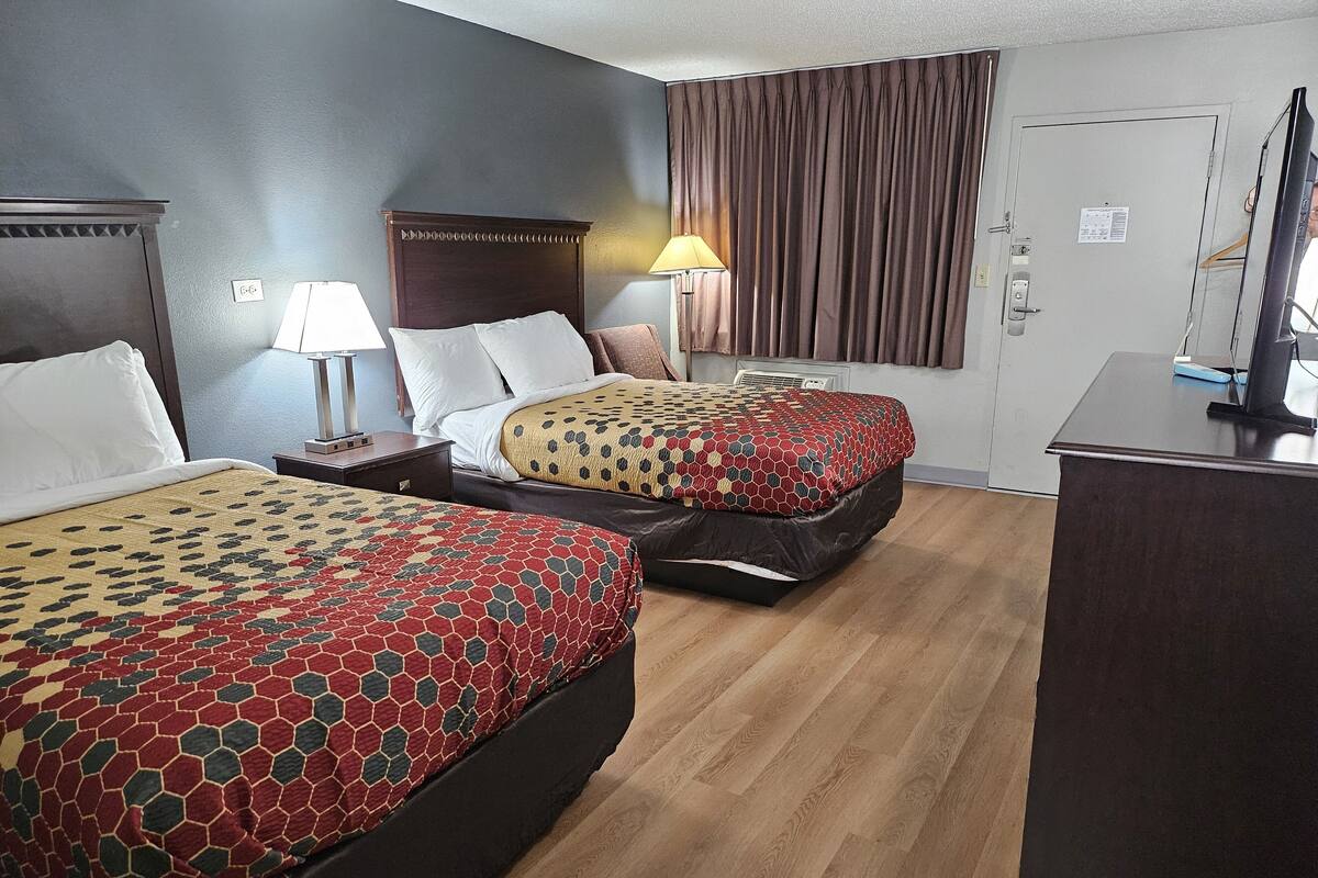 A hotel room with two beds, a desk, a lamp, and a window with curtains.