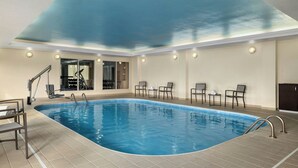 Une piscine intérieure offrant une vue dégagée sur le plafond, un espace détente avec des chaises et des tables, et une porte vitrée donnant sur une autre pièce.