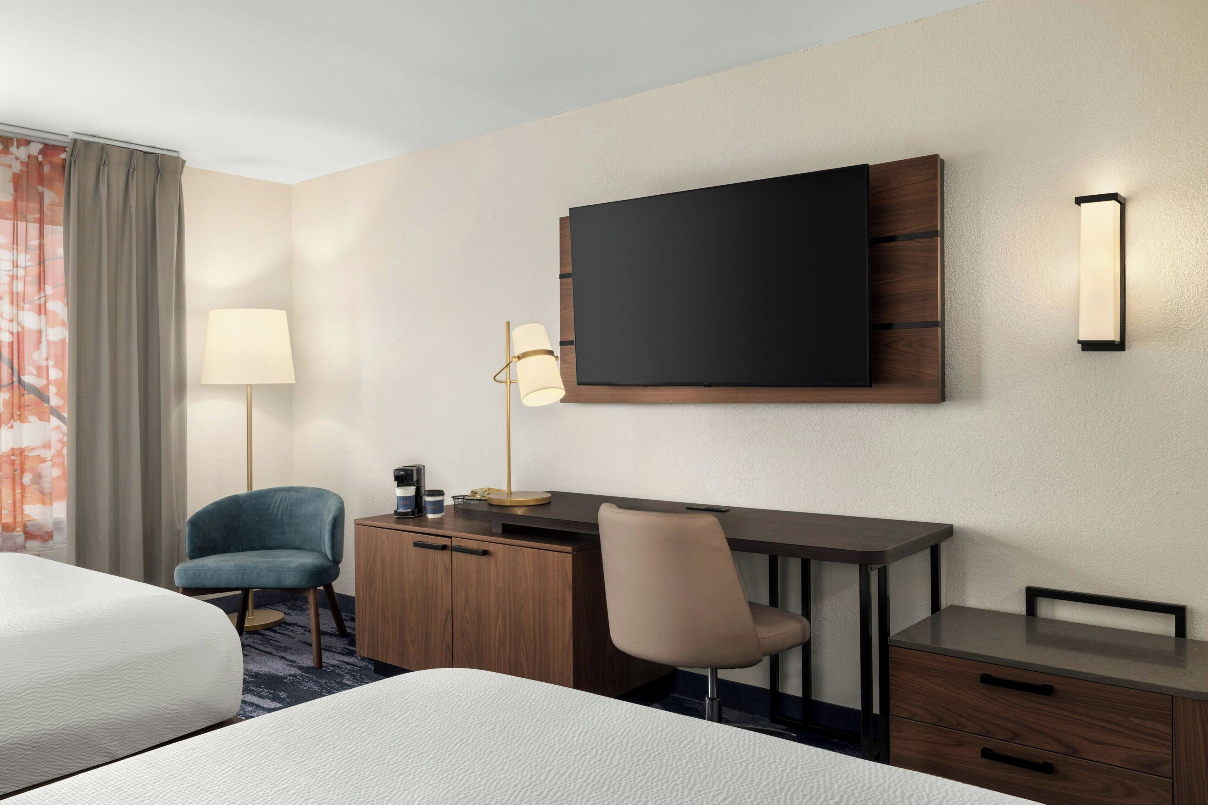 Ein Hotelzimmer mit Bett, Schreibtisch, Stuhl, Flachbildfernseher, Lampe und Kleiderschrank.