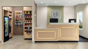 Un comptoir d’accueil d’hôtel avec un distributeur automatique, des étagères de collations et un élément décoratif mural.