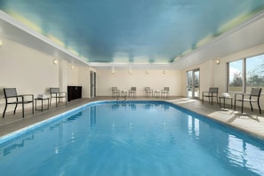 Ein Hallenbad mit Stühlen und Tischen, großen Fenstern und einer Decke mit Farbverlauf in Blau und Grün.