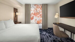 Une chambre d’hôtel avec un lit, un bureau, une chaise, une télévision et une fenêtre avec des rideaux.