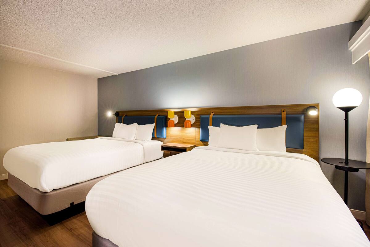 A hotel room with two single beds, a wooden headboard, a nightstand, and a bedside lamp.