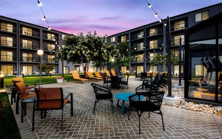A courtyard with outdoor seating, a large building with multiple balconies, and string lights.